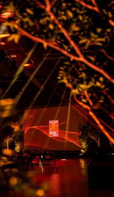 VISUELL Szenografie: BEST CARS 2023: Eine Leinwand im Detail, im Vordergrund ein Baum - alles in rotem Licht umhüllt