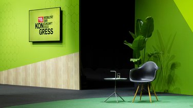VISUELL Szenografie: Bühnenbild und Gesamtinszenierung: Detailaufnahme, ein schwarzer Stuhl mit Beistelltisch stehen vor dem grünen Bühnenbild