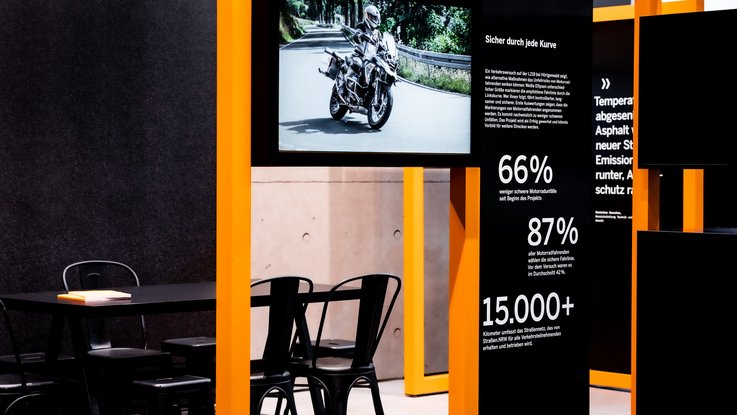 VISUELL Szenografie: Messestand Straßen.NRW auf der InfraTech 2026 VISUELL Szenografie: Messestand Straßen.NRW InfraTech 2026: Ausschnitt zeigt modulares Ausstellungssystem sowie einen Tisch mit Stühlen dahinter; ein integrierter Screen zeigt einen Themenfilm, flankiert von Infopaneelen mit prägnanter Typografie und statistischen Daten.