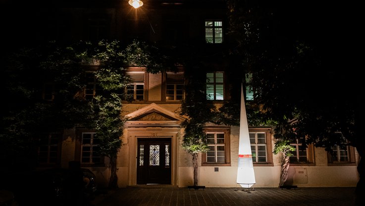 VISUELL Szenografie: Nacht des offenen Denkmals: Ein Leuchtkegel mit Banderole steht vor einem Gebäude