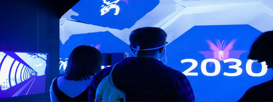 VISUELL Szenografie: Escape-Ausstellung: Besucher stehen im blauen Zeitzug auf dem Weg ins Jahr 2030
