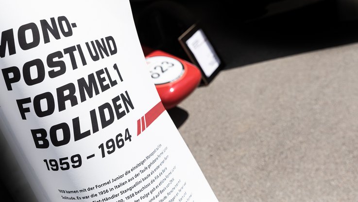 VISUELL Szenografie: Solitude Ausstellung: Stoffbanner mit großer Aufschrift: Monofosti und Formel1 Boliden 1959-1964