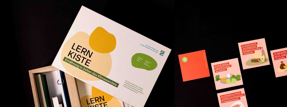 VISUELL Szenografie: Pädagogische Lernkiste: Deckel der Holzkiste mit grün und gelben organischen Elemente- Aufschrift: Lernkiste, Ernährung in Zeiten des Klimawandels